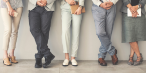 professionally dressed men and women lined up against a wall. We just see their lower body
