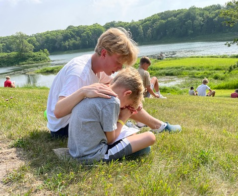 Counselor praying with a kid on a grassy hill