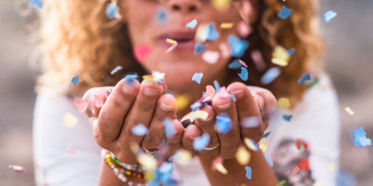 A woman blowing confetti at the viewer from their hands